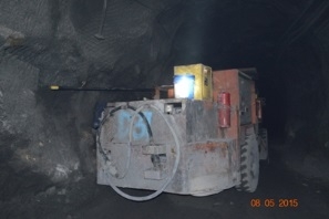 Underground and against a wall lies a machine cart with a long drill installed.