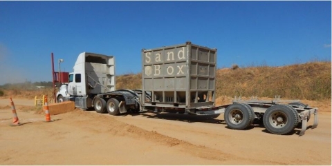White Truck with a trailer with a steal sand box on it.