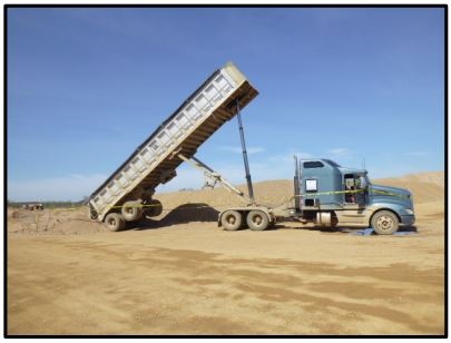 Accident scene where an independent owner/operator truck driver, walked behind his raised end-dump trailer, while dumping his load and was engulfed by sand.