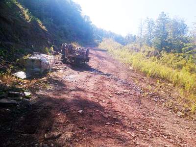 A small upside down truck on a steep roadway. The bed, once hauled by the truck, had fallen to the side of the road in a ditch.