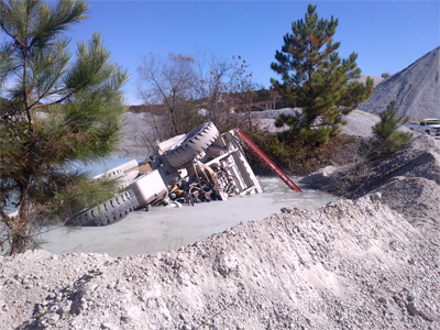 An overturned haul truck in a settling pond that is divided by a berm.