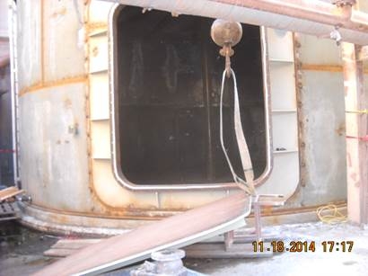 A filtrate tank with a open door way. The door, which landed on the victim, is resting on the floor in front of the tank.