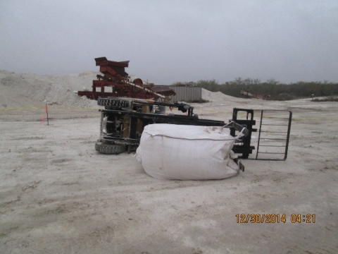 An overturned forklift with a bag that it was hauling still attached to its teeth